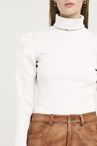 Col roulé blanc à côtes avec des manches bouffantes, associé à un pantalon en cuir marron. Présente une texture subtile et un design ajusté.