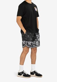 Zwart katoenen T-shirt met een kleurrijke afbeelding, gecombineerd met zwarte shorts met paisleyprint en zwarte sneakers met witte accenten en sokken.