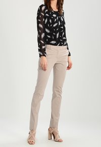 Black, sheer blouse with white feather pattern; light beige slim-fit pants; strappy nude high-heeled sandals. Smooth, lightweight fabric.