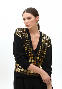 Black sweater with a deep V-neck, featuring gold circular sequins along the shoulders and down the front, in a soft texture.