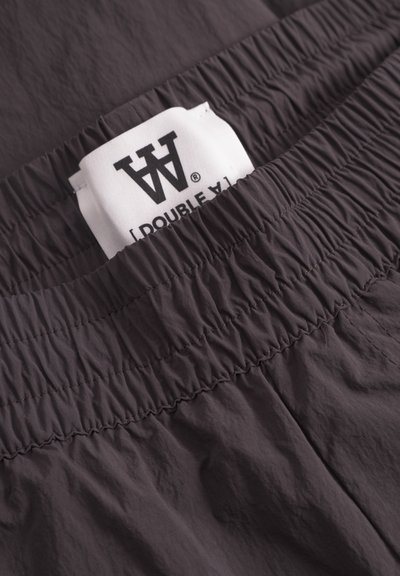 Ceinture élastique gris foncé avec texture froncée, présentant une étiquette en tissu blanc visible avec un texte noir indiquant "[DOUBLE A]".
