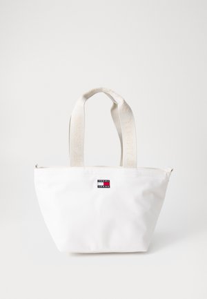 White tote bag made of smooth fabric, featuring a zip closure, flat bottom, and logo patch, with cream handles labeled "TOMMY JEANS."
