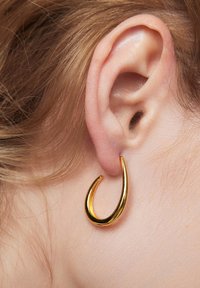 Złoty, zakrzywiony klips na ucho przedstawiony na uchu, z gładkim, błyszczącym wykończeniem i minimalistycznym wzornictwem.