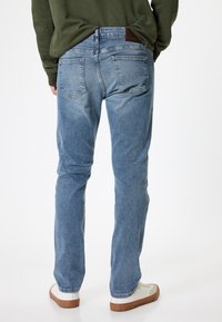 Lyseblå denimjeans med lige pasform, fem lommer og en læderlap på rygsløjfen. Båret med hvide sneakers.