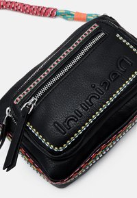 Musta nahkainen olkalaukku, jossa on teksturoitu pinta, kontrastivärillä ommellut yksityiskohdat ja hopeinen vetoketju. Yksityiskohtina punottu olkahihna.