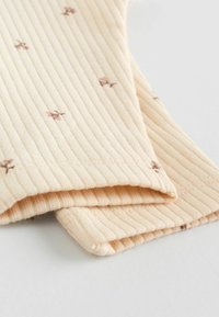 Tissu côtelé beige avec des motifs floraux en brun clair. Deux couches repliées l'une sur l'autre, mettant en valeur une texture douce et un design subtil.