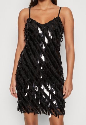 Woman wearing sleeveless black mini dress with diagonal rows of shiny black sequins and fringe details.