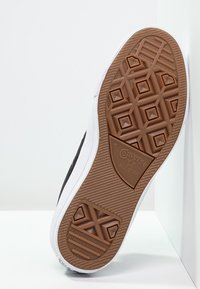 Černé plátěné tenisky s bílou gumovou podrážkou a vzorovanou hnědou podešví, s logem "Converse All Star". Viditelné detaily texturovaného povrchu.