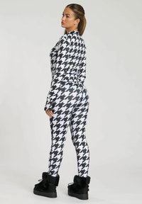 Black and white houndstooth-patterned two-piece set with long sleeves, fitted leggings, and soft, textured black footwear.