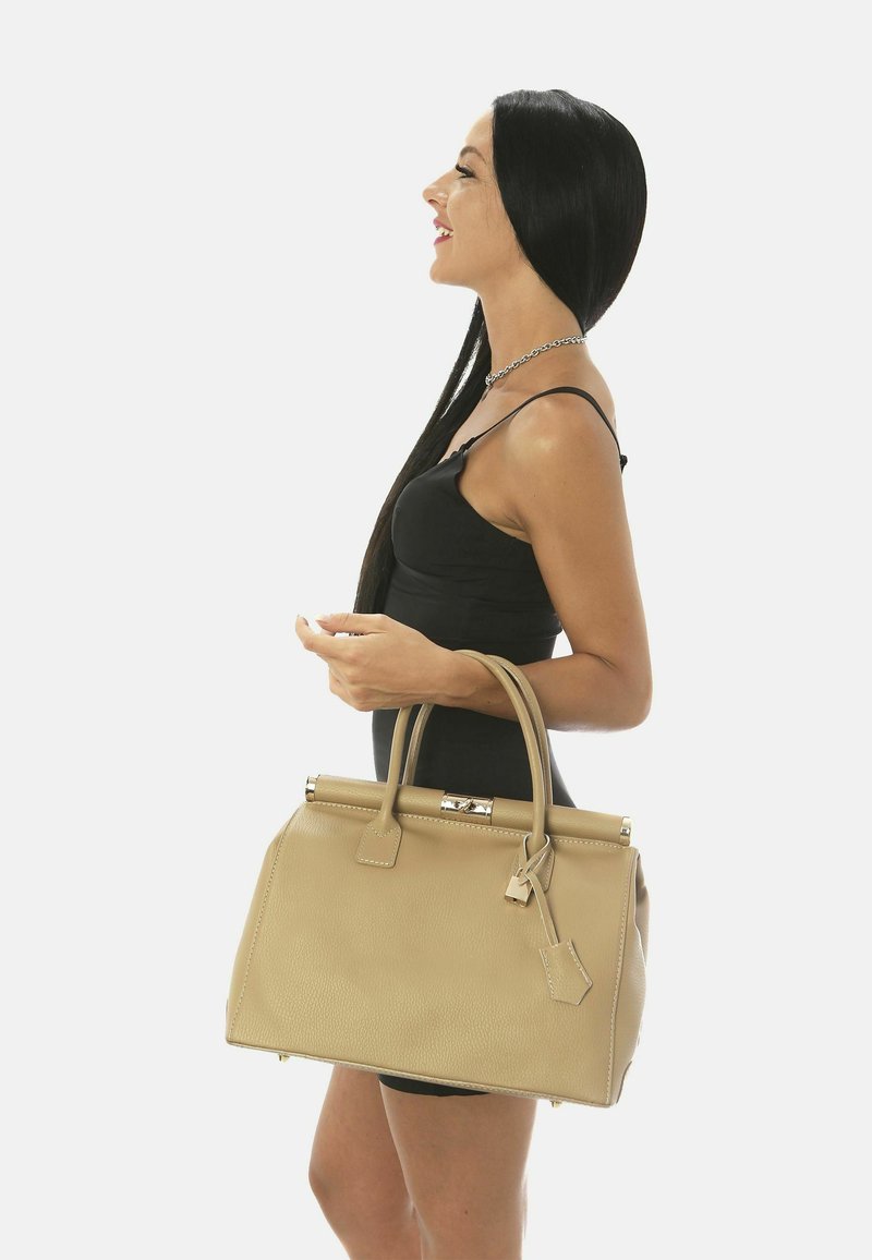 Beige läderhandväska med en strukturerad design, dubbla handtag och en låsfunktion. Slät yta och glänsande metalldetaljer.