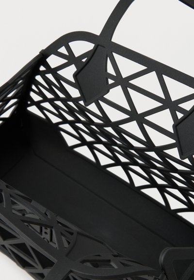 Μαύρη γυναικεία τσάντα με γεωμετρικό σχέδιο κοπής και δύο λαβές σε λευκό φόντο.