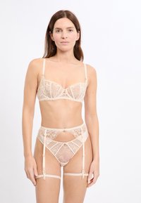 Lace beha- en jarretelset in naaktkleur, met doorschijnende stof, bloemmotieven, beugelondersteuning en verstelbare bandjes. Gedetailleerd met satijnen accenten.