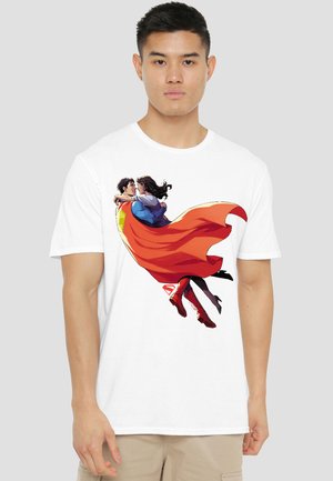 Man wearing white T-shirt with graphic of a flying superhero embracing a woman wrapped in a flowing red cape.