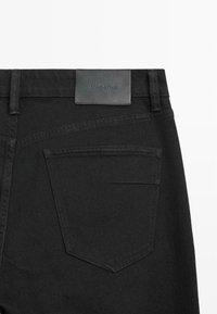 Czarne dżinsy z denimu z skórzaną naszywką z logo "Massimo Dutti", standardową tylną kieszenią oraz kontrastowym przeszyciem wzdłuż linii talii.