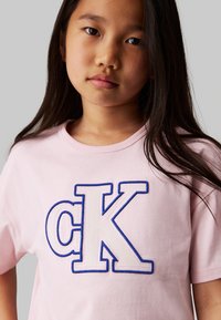 T-shirt di cotone rosa con grande ricamo "CK" bianco e blu. Maniche corte e scollatura rotonda. Texture liscia.