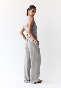 Graues Zweiteiler-Outfit mit einem kurz geschnittenen Top mit Rückenschnürung und lockeren, hoch taillierten, weit geschnittenen Hosen mit Taschen aus strukturiertem Stoff.