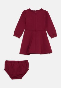 Vestido longo bordeaux de mangas longas com decote redondo e fecho nas costas, apresentando uma saia rodada, combinado com calções ajustáveis à cintura.