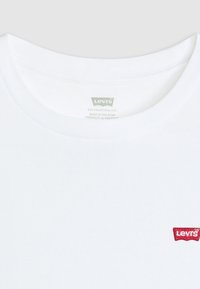 Bílé tričko s krátkými rukávy a kulatým výstřihem. Na levé straně hrudi je červené logo Levi's ve formě štítku. Hladká bavlněná látka, minimalistický design.
