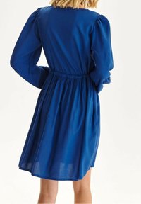 Sininen mekko, jossa on pitkät puff-hihat ja kapea vyötärö. Valmistettu kevyestä materiaalista, jossa on valuvat helmakaudet ja sileä rakenne.