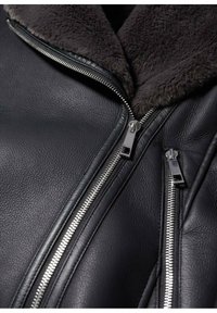 Czarna skórzana kurtka z miękkim, ciemnym futrzanym kołnierzem i srebrnymi detalami zamka błyskawicznego. Faktura skórki podkreśla subtelny wzór ziaren.