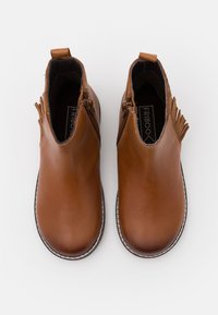 Hnědé kožené kotníkové boty s bočními zipy, texturovanými akcenty a prošívaným bílým okrajem kolem černé podešve.