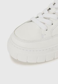 Baskets en cuir blanc avec une semelle épaisse, un bout arrondi et des lacets blancs. Présente des détails de couture et une texture lisse.