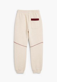 Crème-kleurige joggingsbroek met een elastische tailleband, voorzien van een kastanjebruine accentzak en contrasterende stiksels langs de benen.