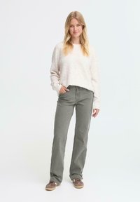 Suéter texturizado rosa claro con puños acanalados, combinado con pantalones rectos grises y zapatos marrones. Diseño sencillo y materiales suaves.