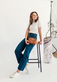 Brown quilted crossbody bag with a chain strap, featuring a chevron design. Model wearing a white top and blue wide-leg jeans.