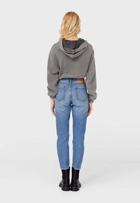 Sudadera gris corta con capucha ajustable, combinada con jeans ajustados de tiro alto en azul y botas negras. Texturas suaves y diseño casual.