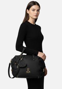 Borsa a mano in pelle nera con dettagli in oro, forma arrotondata, finitura testurizzata, dettaglio logo e ciondolo a forma di cuore staccabile.