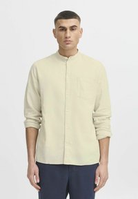 Helles beige Langarmhemd mit Bandkragen, Knopfleiste vorne und einer Brusttasche, aus einem weichen, strukturierten Stoff.
