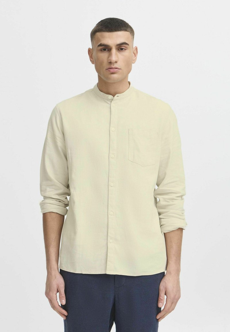 Helles beige Langarmhemd mit Bandkragen, Knopfleiste vorne und einer Brusttasche, aus einem weichen, strukturierten Stoff.