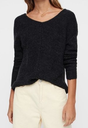 Femme portant un pull en maille côtelée gris foncé avec un col en V et des manches longues, associée à un pantalon taille haute écru.