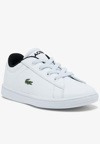 White low-top sneaker with white laces, black inner lining, and green crocodile logo on the side.