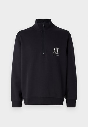 Musta poolapainen huppari, jossa on korkea kaulus ja neljännesvetoketju. Vasemmassa rinnassa on valkoinen logo sekä resorit hihansuissa ja helmoissa.