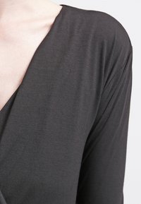 Czarny, lekki top z dzianiny z głębokim dekoltem w kształcie litery V i długimi rękawami. Materiał ma gładką teksturę i miękko układa się na skórze.