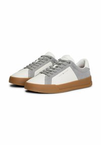 Sneaker basse con tomaia in pelle bianca e suede grigio, lacci grigi e suola in gomma marrone. Presentano un branding minimale sul lato.