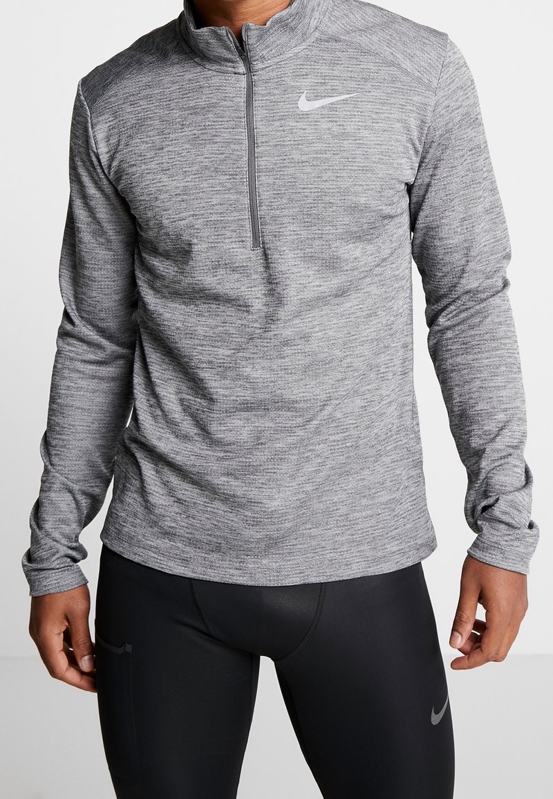 Pullover sportivo con zip a metà, realizzato in tessuto grigio misto. Presenta una leggera trama e un logo Nike sul lato sinistro del petto.