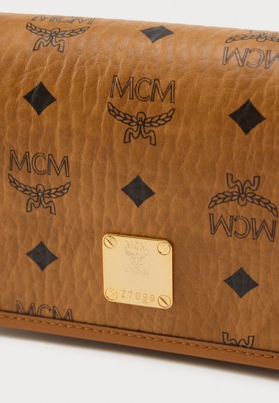 Καφετί δερμάτινο πορτοφόλι με μαύρα λογότυπα MCM και διαμάντια. Περιλαμβάνει χρυσή πλακέτα με χαραγμένες λεπτομέρειες και ραμμένα άκρα.