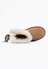 Bota de ante en color marrón claro con un suave forro de piel de oveja blanca, punta redonda y un detalle de cordones con estampado de leopardo en el tobillo para un ajuste seguro.