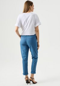 T-shirt blanc court avec des manches retroussées associé à un pantalon bleu fuselé et des talons noirs à lanières, avec un tissu lisse et un design minimaliste.