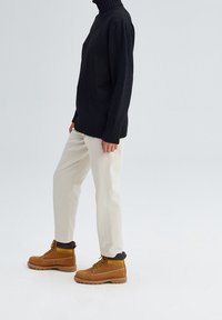 Czarny sweter z golfem i prążkowanym dół, kremowe spodnie oraz brązowe buty z żółtymi i czarnymi akcentami, prezentujące casualowy strój.