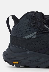 Scarpa da trekking nera con tomaia texturizzata, mesh traspirante e suola Vibram. Presenta un tallone rinforzato e accenti grigi a contrasto.