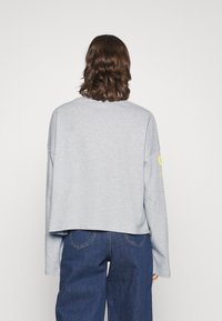 Light gray cropped sweatshirt with long sleeves, featuring a round neck and a yellow graphic on the left sleeve. Soft cotton material.