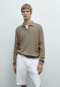 Hnědý dlouhý rukáv polo svetr s límečkem a manžetou, v kombinaci s bílými lněnými šortkami. Materiál vypadá měkký s jemnou strukturou.