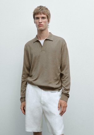 Maglione polo a maniche lunghe marrone con colletto e patta, abbinato a pantaloni corti bianchi in lino. Il tessuto sembra morbido con una sottile texture.