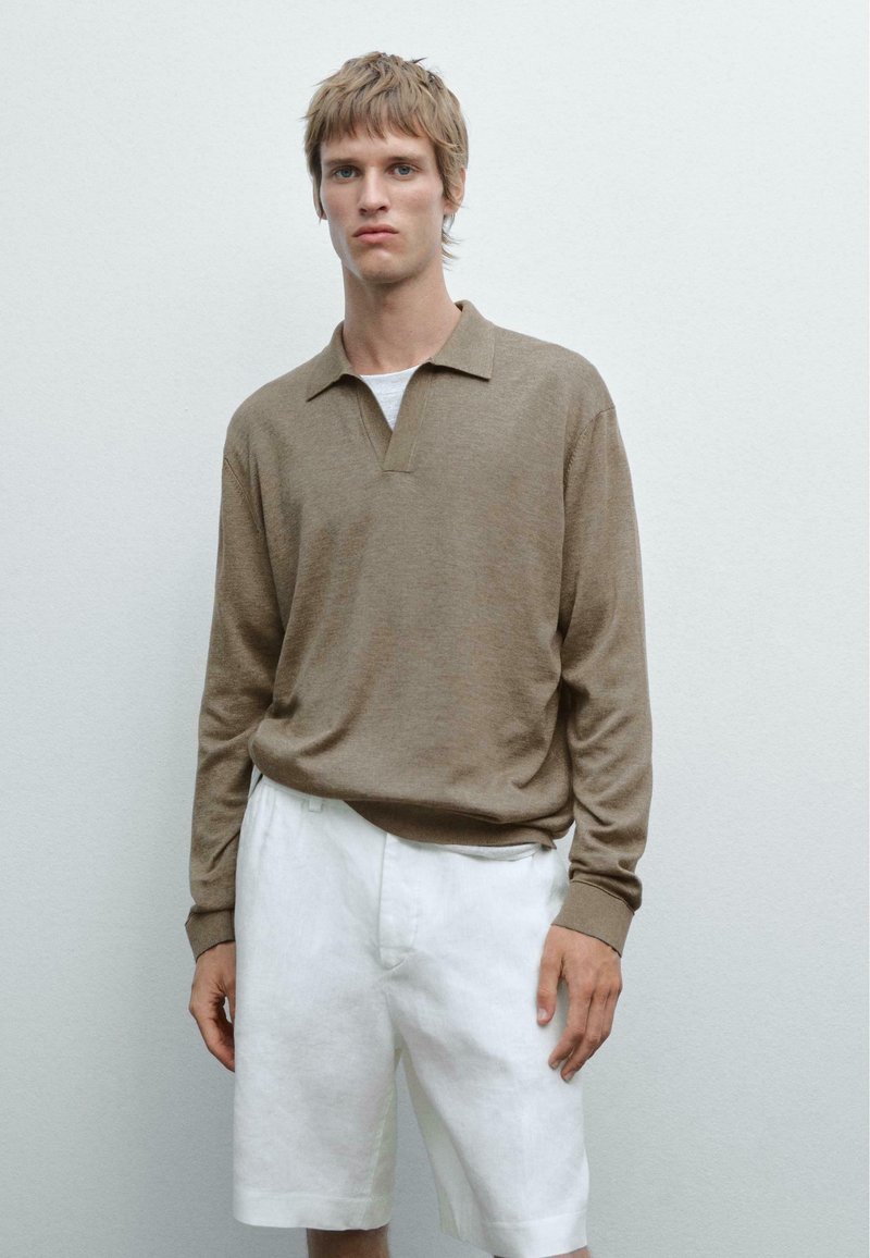 Hnědý dlouhý rukáv polo svetr s límečkem a manžetou, v kombinaci s bílými lněnými šortkami. Materiál vypadá měkký s jemnou strukturou.
