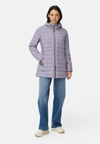 Doudoune légère violette avec capuche, dotée de matelassage horizontal, fermeture éclair sur le devant et deux poches latérales. Associée à un jean bleu et des baskets blanches.