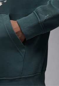 Sudadera de color teal con bolsillo tipo canguro, puños acanalados y un logo Jumpman bordado en la manga. Acabado de tela suave y texturizada.